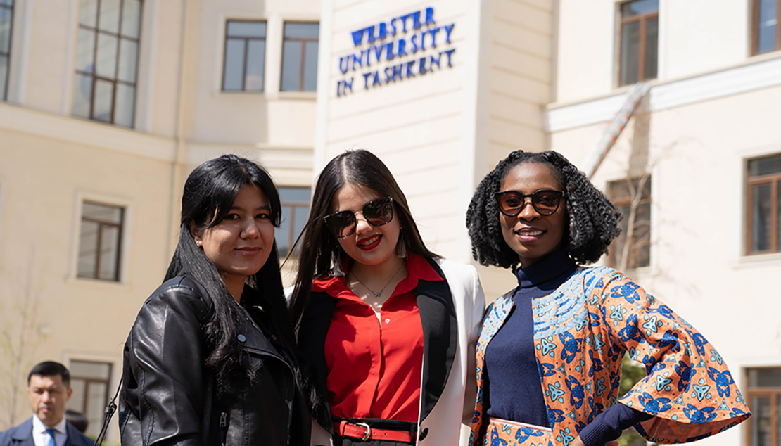 Three women stand together in front of ĻӰ Tashkent sign with a man standing to the side of them..